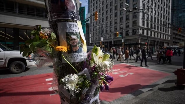 Une photo d'un jeune homme et la mention RIP (repose en paix) et des fleurs sont posées sur un poteau.