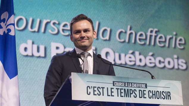 Paul St-Pierre-Plamondon debout derrière un lutrin devant une affiche du Parti québécois. 