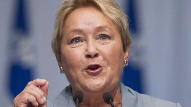 Pauline Marois en gros plan parle dans deux micros d'un air déterminé.