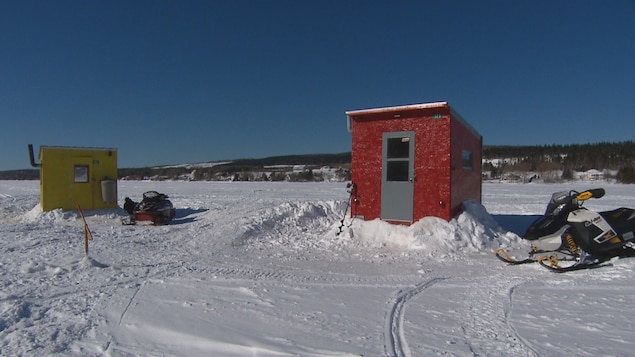 Deux cabanes sur le lac glacé. Des motoneiges sont stationnées tout près.