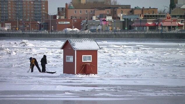 Deux personnes installent leur cabane sur la banquise, face au centre-ville de Rimouski.