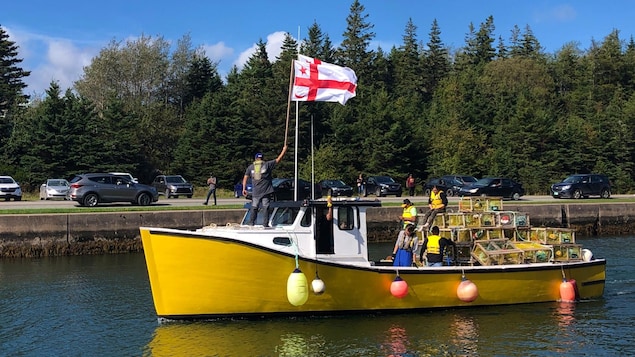 Le drapeau mi'kmaw flotte sur un petit bateau de pêche jaune qui quite le quai.