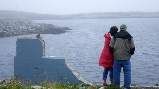Deux personnes se tiennent près des décombres de leur ancienne maison, non loin de la mer.