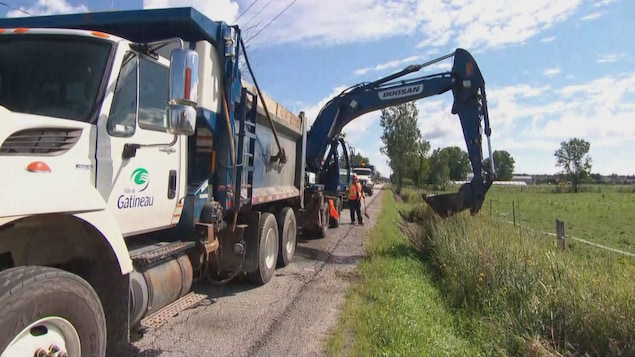 Une pelle mécanique creuse dans un fossé en bordure d'une route à Gatineau.