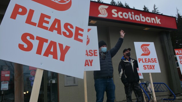Des gens tiennent des pancartes devant une Banque Scotia.