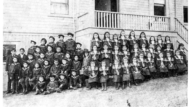 Un groupe d'enfants en uniformes pose devant une école.
