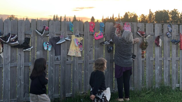 Une femme pose un porte-bébé sur la clôture et deux jeunes enfants s'approchent en courant.
