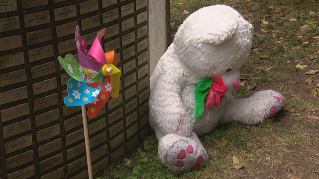 Un ourson en peluche blanc et un vire-vent devant une plaque avec des noms