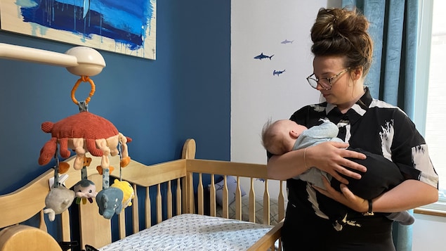 Une femme près d'un berceau, dans une chambre d'enfant, tient dans ses bras un bébé et le regarde.
