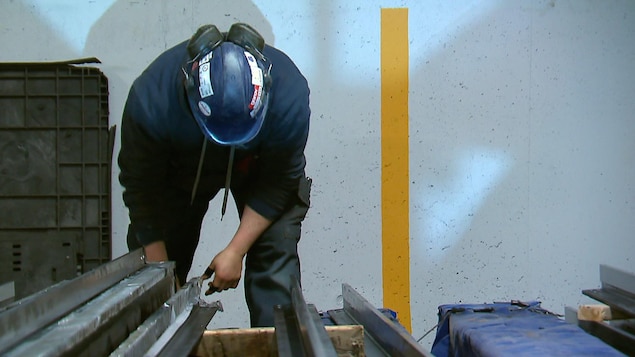 Un employé d'une entreprise d'installation d’ascenseurs en train de couper des pièces de métal.