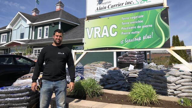 Dany Desgranges se tient debout devant la façade de l'entreprise. Plusieurs sacs de terres sont empilés sur le terrain.