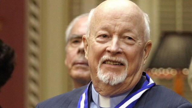 Gros plan du père Johns portant un col romain et la médaille de l'Ordre national du Québec.