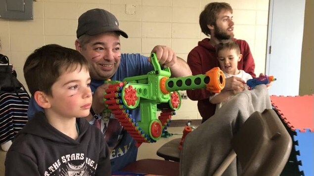 En avant plan un homme tenant une arme en plastique prêt a tirer et devant lui son enfant qui tient un pistolet en plastique