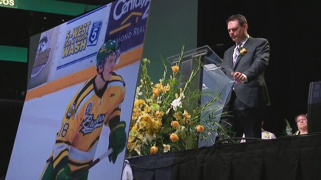 Le père de Logan Hunter, Lawrence Hunter, au podium devant une photo de son fils en tenue de hockey. Le père de Logan Hunter, Lawrence Hunter, au podium devant une photo de son fils en tenue de hockey.