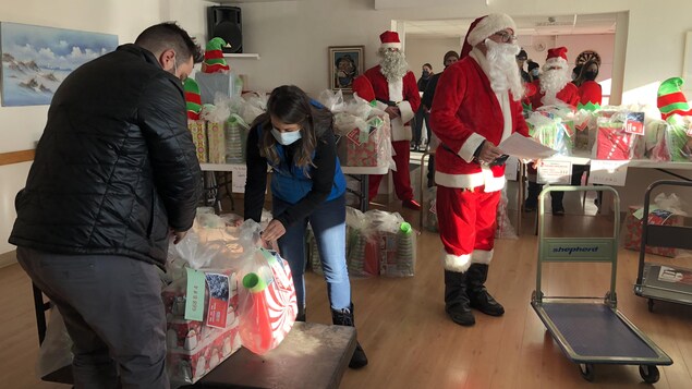 Une salle remplie de boites cadeau. On y voit trois pères Noël.