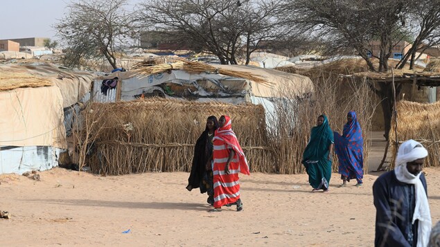 Des personnes marches dans un camp de déplacés internes sur un sol aride.