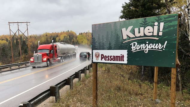 Une affiche qui souhaite la bienvenue sur la communauté de Pessamit. On voit la route 138 derrière.