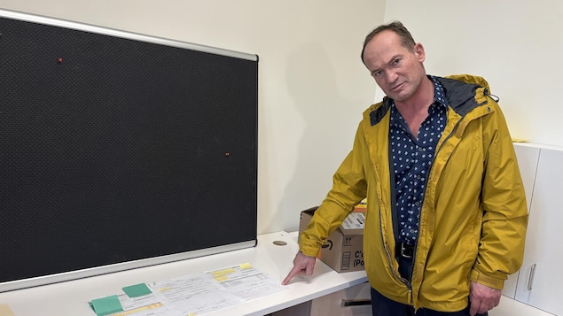 Un homme avec un manteau jaune et chemise bleu pointe un document sur une table