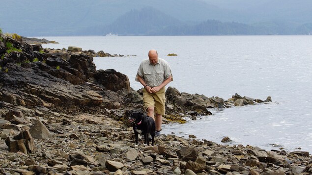 Peter Lake marche sur le bord de l'eau avec son chien noir. Peter Lake marche sur le bord de l'eau avec son chien noir.