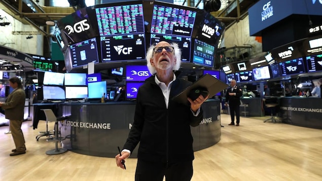 Peter Tuchman, clipboard in hand, looking at various screens on the floor of the New York Stock Exchange.