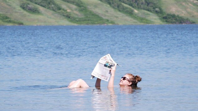 Une femme flotte sue le lac Petit-Manitou en lisant le journal.