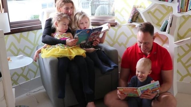 Une mère tient ses deux filles et leur lit un livre. Un père est assis par terre et lit également un livre à son jeune enfant. Ils sont ensemble dans une pièce ensoleillée. Une mère tient ses deux filles et leur lit un livre. Un père est assis par terre et lit également un livre à son jeune enfant. Ils sont ensemble dans une pièce ensoleillée.