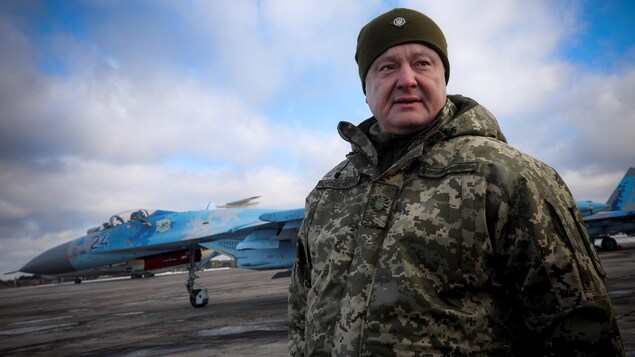 Petro Porochenko pose en habit de camouflage sur un tarmac, un avion militaire se trouve derrière lui.