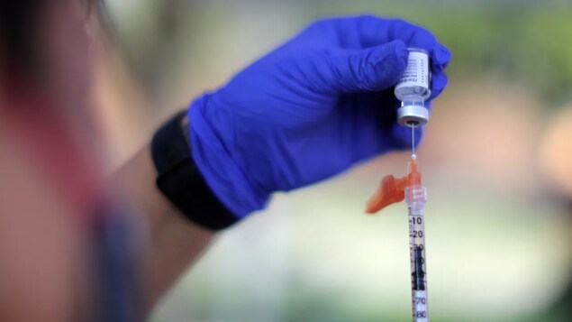 Kamay hawak ang isang vial na may nakatusok na hiringgilya.