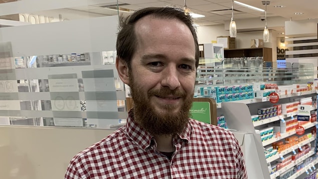 Michaël Tourigny pose devant un panneau explicatif de ce qu'est une pharmacie carboneutre. 