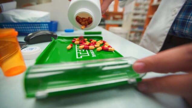 Pills on a tray are being handled by someone at a pharmacy.