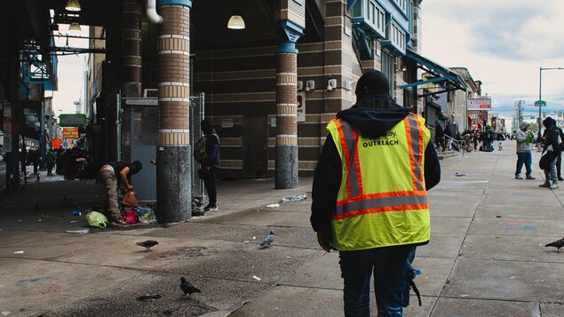 Un travailleur de rue marche en direction d'une station de métro. Des dizaines de sans-abri et de consommateurs de drogue sont installés dans la rue.