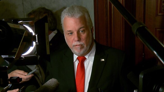 Le premier ministre du Québec Philippe Couillard debout dans le couloir de l'Assemblée nationale, répond aux questions relativement à la Commission sur le racisme et la discrimination systémique