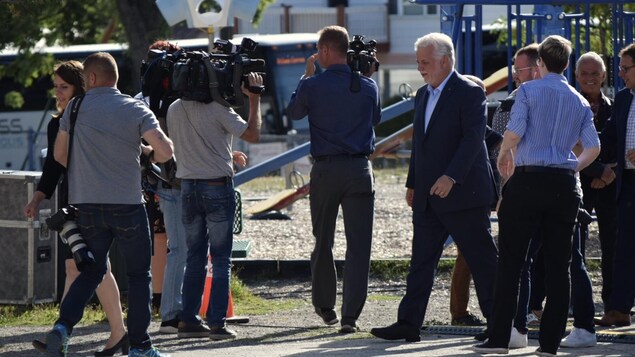 Philippe Couillard sur le terrain d'une école avec des journalistes