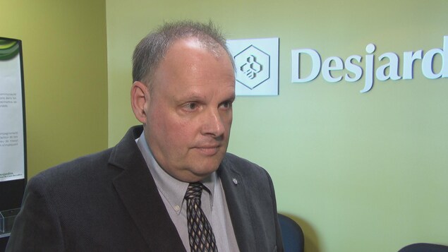 L'homme est interviewé devant un logo de Desjardins. L'homme est interviewé devant un logo de Desjardins.