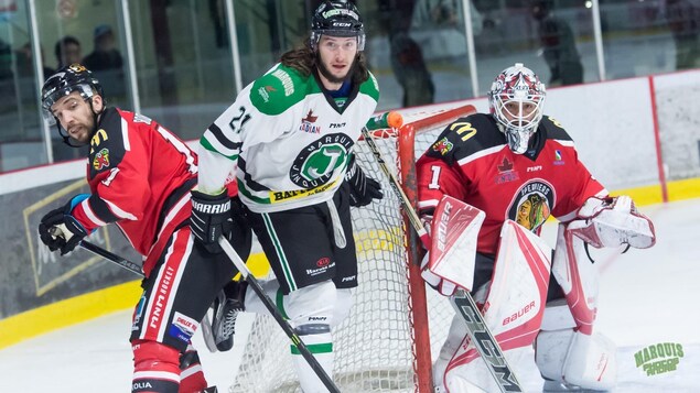 Des joueurs de hockey se trouvent derrière un filet qui est étroitement surveillé par un gardien de but.