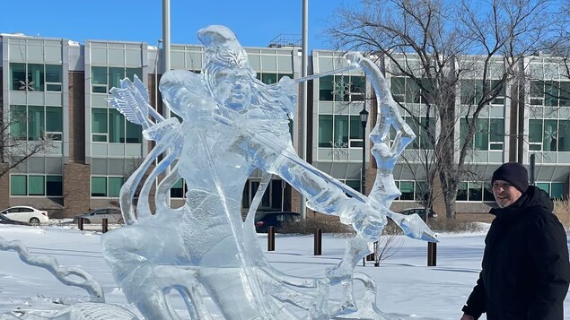 Lalaki nakatayo sa tabi ng malaking ice sculpture ng isang archer.