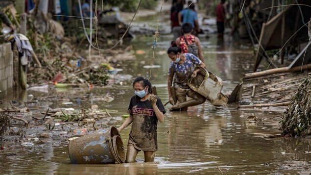 Des Philippines marchent dans des rues inondées, certaines transportant des objets.