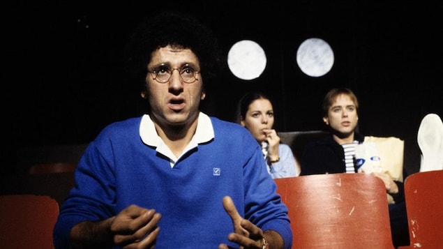 Les trois comédiens sont assis dans différentes rangées d'une salle de cinéma.