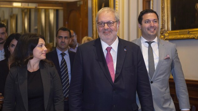 Pierre Arcand marche dans un corridor avec, à ses côtés, la députée Filomena Rotiroti et le président du Parti libéral du Québec, Antoine Abdallah.