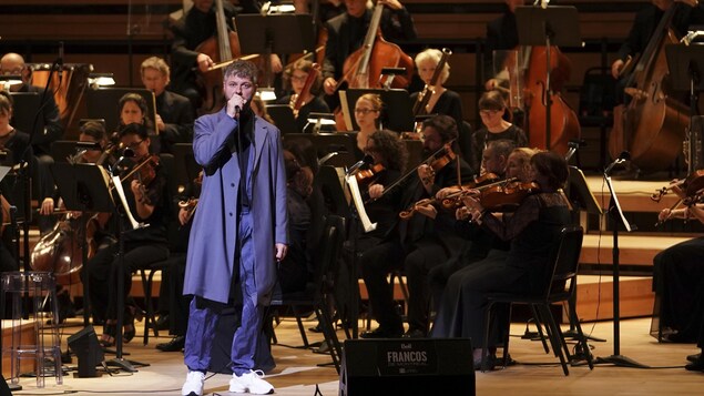 Un chanteur est accompagné d'un orchestre complet sur scène.