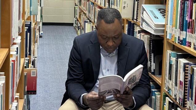 Pierre Minkala-Ntadi lit un livre dans une bibliothèque.