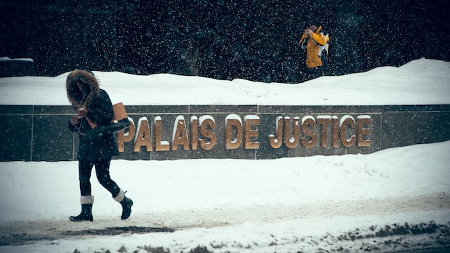 Une femme passe devant l'enseigne du Palais de justice de Montréal, sous une fine neige. Un homme s'allume une cigarette à l'entrée de l'édifice.