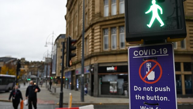 Des piétons à Bradford passent devant un panneau de feux de circulation, qui leur conseille de ne pas utiliser le bouton à cause de la COVID-19.