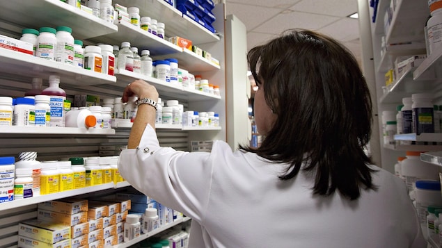 Une technicienne prend une bouteille de pilules sur une des étagères d'une pharmacie.