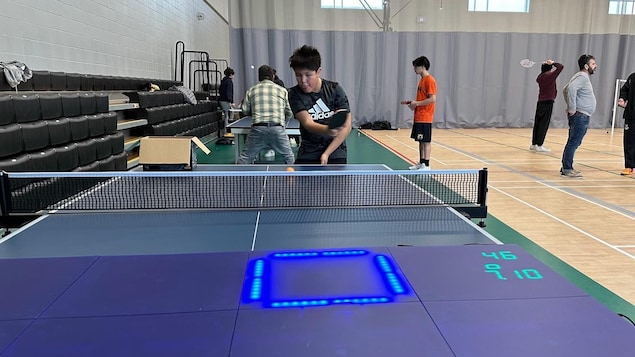 Un élève joue au ping-pong et un tapis électronique est posé sur la table. 