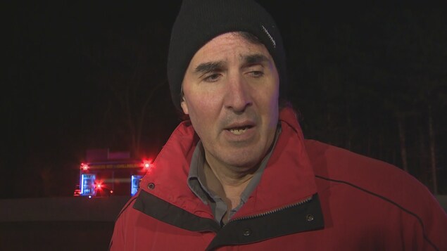 Photo de Vincent Di Pinto, portant un manteau rouge et une tuque noire, un camion de pompier en arrière-plan Photo de Vincent Di Pinto, portant un manteau rouge et une tuque noire, un camion de pompier en arrière-plan