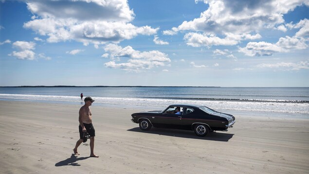 Une voiture rétro passe près d'un homme sur la plage de Crescent Beach, en août 2016.