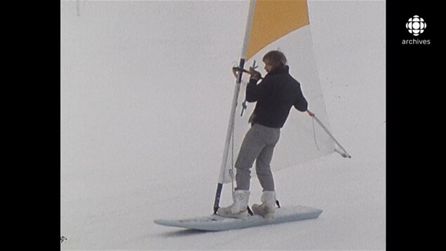Homme glissant sur une planche à voile sur neige sur une surface glacée et légèrement enneigée Homme glissant sur une planche à voile sur neige sur une surface glacée et légèrement enneigée