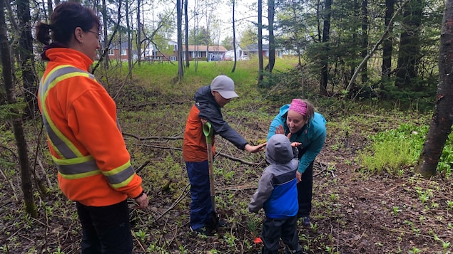 Une mère avec ses deux enfants ont planté un arbre et se félicitent. Une employée de la société des parcs de Baie-Comeau supervise l'activité.
