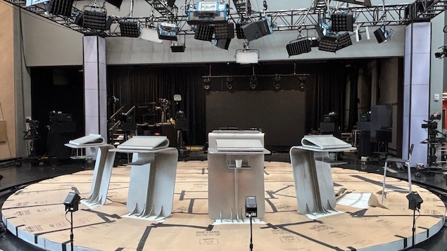 Quatre lutrins placés en demi-cercle sur un plateau de télévision.